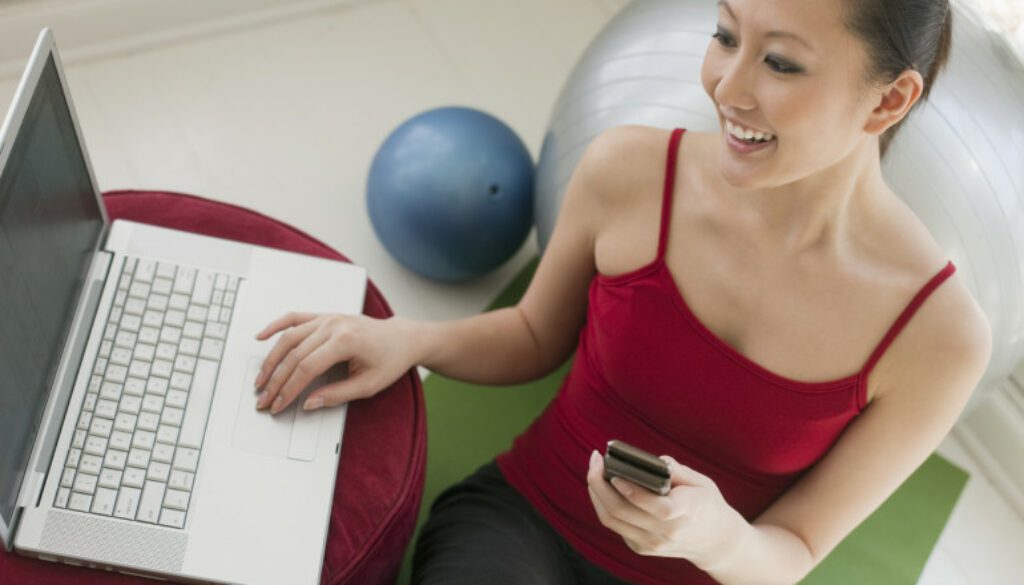 Young Asian woman with cell phone and laptop personal trainers